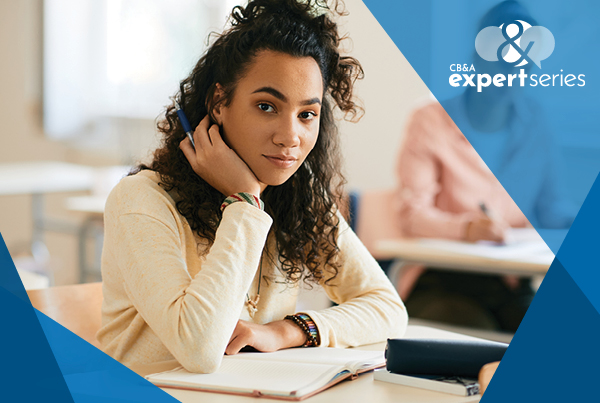 student sitting at classroom desk with chin in hand and neutral expression