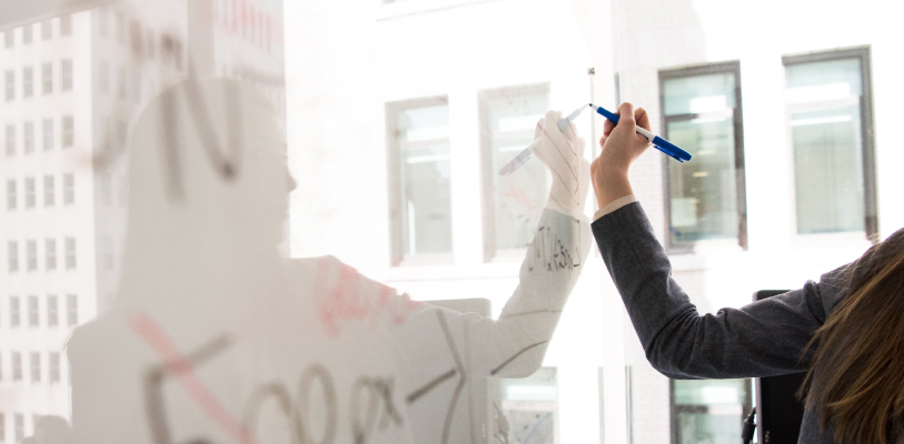 Image of adult writing with their left hand on a large dry erase board.